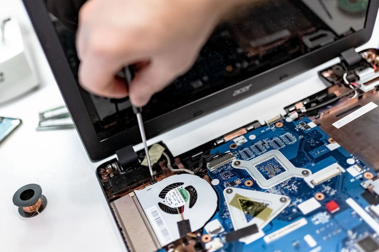 Unes mans desmunten un portàtil amb un tornavís per reparar-lo, amb la placa base a la vista.